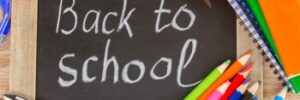 Chalkboard with "Back to school" written on it, surrounded by colorful pens, pencils, and notebooks.