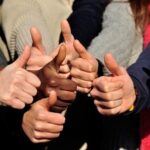 A group of people giving thumbs-up signs, showing various skin tones and wearing different colored clothes.