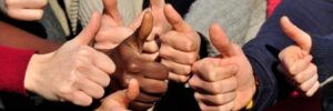 A group of people giving thumbs-up signs, showing various skin tones and wearing different colored clothes.