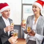 Four people in Santa hats clinking glasses of champagne, dressed in business attire, in a festive indoor setting.