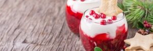 Two dessert glasses with layered red and white parfaits, topped with star-shaped cookies and berries, on a wooden surface.