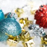 Glittery blue and red Christmas ornaments with small gold and silver gifts on a snowy background.