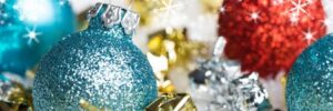 Glittery blue and red Christmas ornaments with small gold and silver gifts on a snowy background.