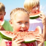 Three children outdoors eating slices of watermelon on a sunny day.