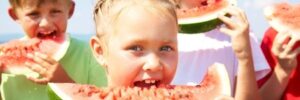 Three children outdoors eating slices of watermelon on a sunny day.