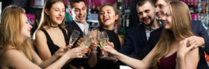 A group of people in formal attire clinking glasses and smiling in a bar setting.