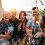 Five people celebrating outdoors, smiling and holding party poppers, with confetti in the air.