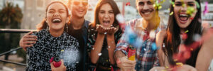 Five people celebrating outdoors, smiling and holding party poppers, with confetti in the air.