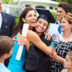 A graduate in cap and gown is hugged by family and friends, celebrating together outdoors.