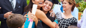 A graduate in cap and gown is hugged by family and friends, celebrating together outdoors.