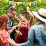 A group of people dancing outdoors at a festive gathering, with colorful bunting in the background.