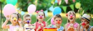 Children at a table wearing clown noses with balloons and party decorations in the background.