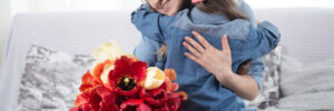 Woman and child embracing on a sofa, smiling, with a bouquet of red and yellow flowers in the foreground.