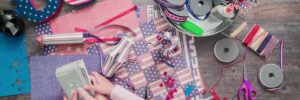 Hands organizing patriotic crafts with ribbons, paper, and USA letters on a wooden table.