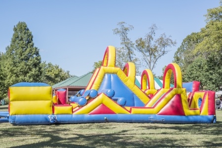 Colorful inflatable obstacle course on grass with trees and a building in the background under a clear sky.