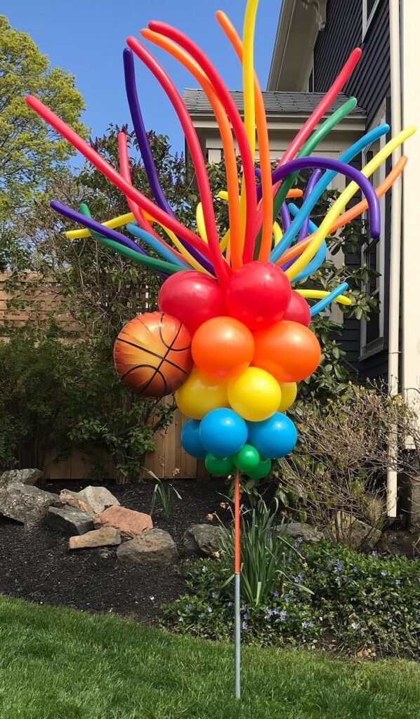 Colorful balloon sculpture with a basketball design in a garden setting.