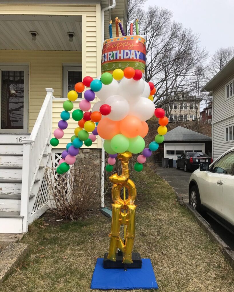 Colorful balloon display with "Happy Birthday" decoration and golden "100" in front of a house.