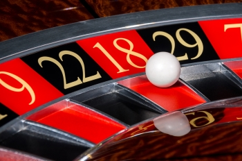 Close-up of a roulette wheel with a white ball landing on the number 18, surrounded by black and red numbered slots.