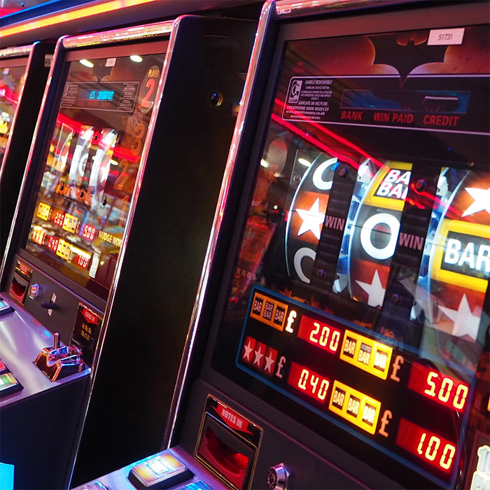 An example of a row of illuminated gambling slot machines with spinning reels displaying symbols and numbers in a casino setting.